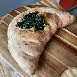 Folded calzone filled with cheese and spinach on top.