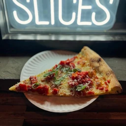 A slice of Grandma-style thin-crust pizza with tomatoes and basil.